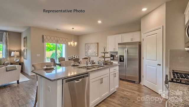 kitchen featuring light wood-type flooring, pendant lighting, an island with sink, appliances with stainless steel finishes, and sink