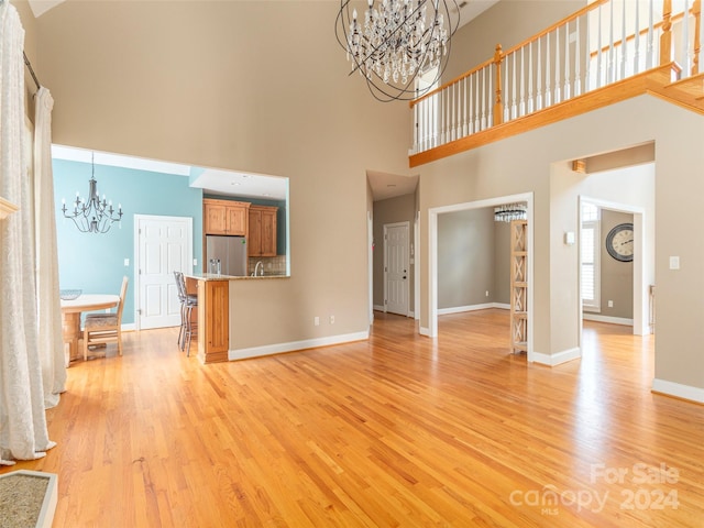 unfurnished living room featuring a high ceiling, a notable chandelier, and light hardwood / wood-style floors