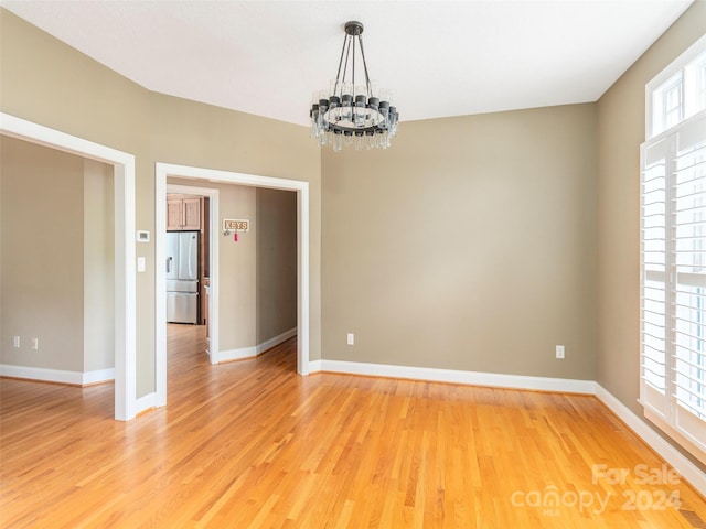 unfurnished room featuring an inviting chandelier and light hardwood / wood-style floors