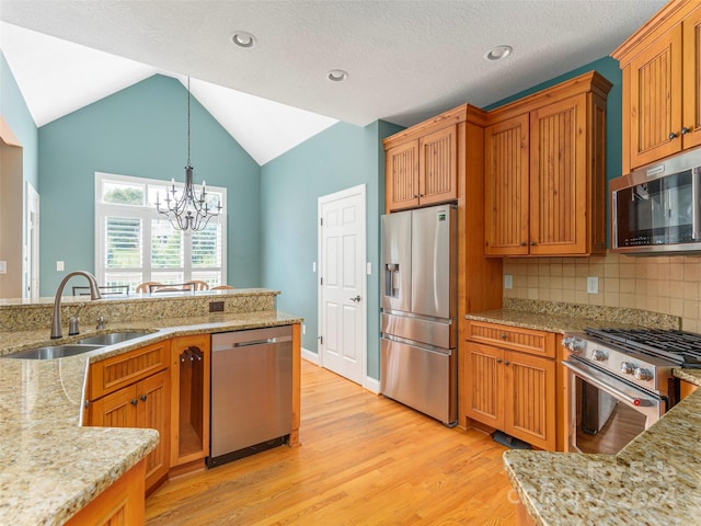 kitchen featuring light stone countertops, a notable chandelier, appliances with stainless steel finishes, sink, and light wood-type flooring