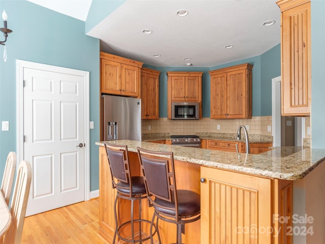 kitchen featuring tasteful backsplash, a kitchen bar, kitchen peninsula, light wood-type flooring, and premium appliances