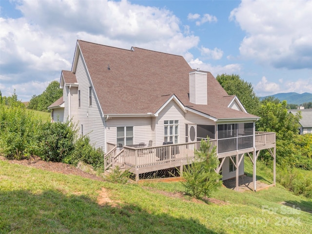 back of property featuring a chimney, a deck, a shingled roof, a sunroom, and a yard
