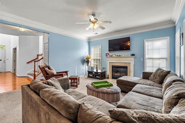 living area with a fireplace with flush hearth, a ceiling fan, ornamental molding, baseboards, and stairs