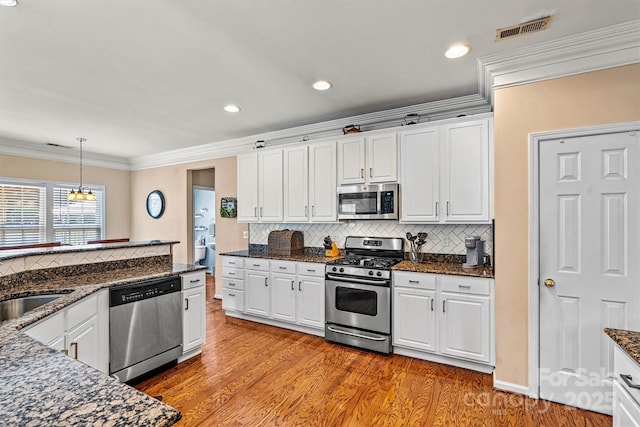 kitchen featuring visible vents, light wood-style floors, white cabinets, appliances with stainless steel finishes, and crown molding