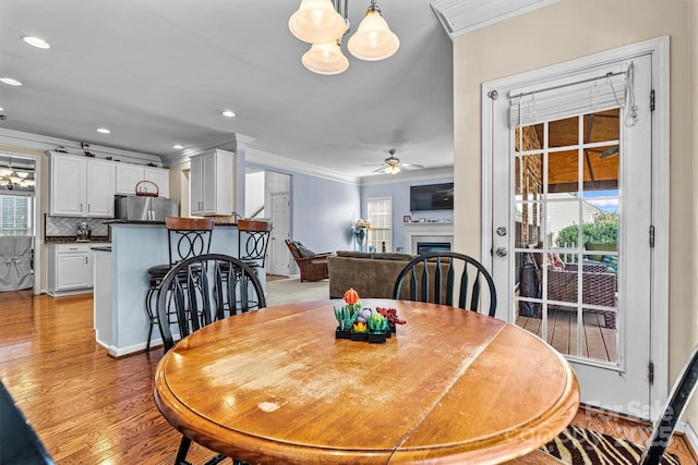 dining space featuring ornamental molding, light wood-style floors, a fireplace, and a ceiling fan