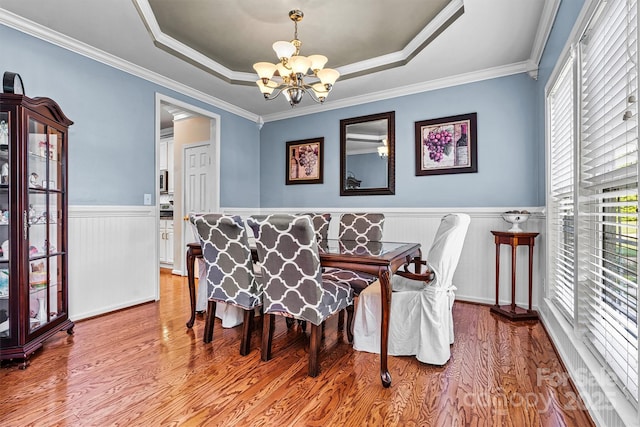 dining room with a wainscoted wall, wood finished floors, a raised ceiling, and an inviting chandelier