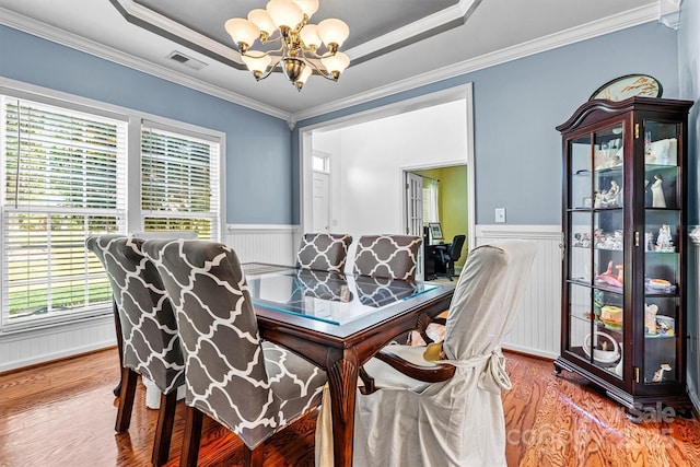 dining area featuring a chandelier, a tray ceiling, wainscoting, and wood finished floors