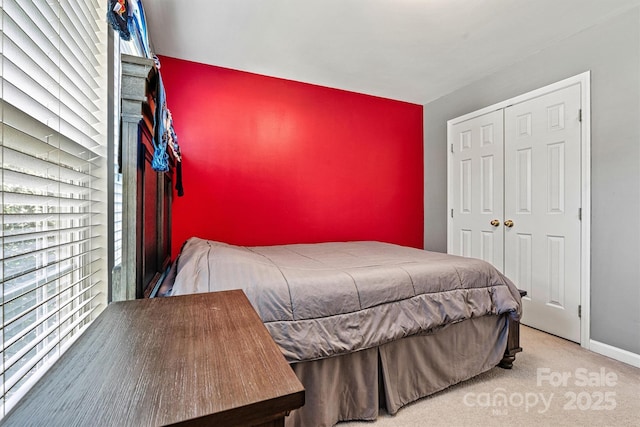 carpeted bedroom with an accent wall, a closet, and baseboards