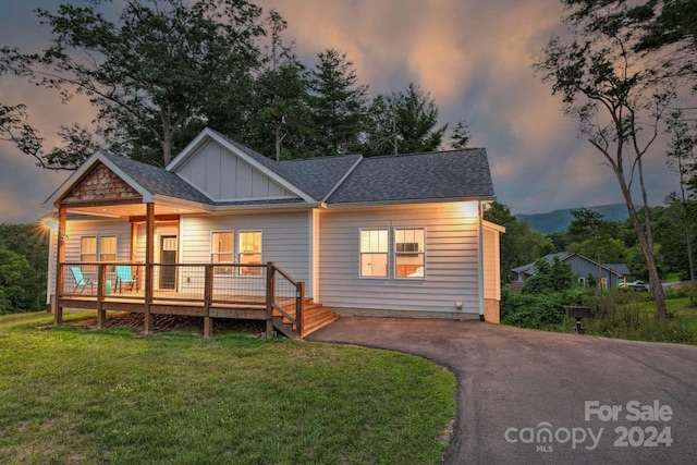 back house at dusk featuring a wooden deck and a lawn