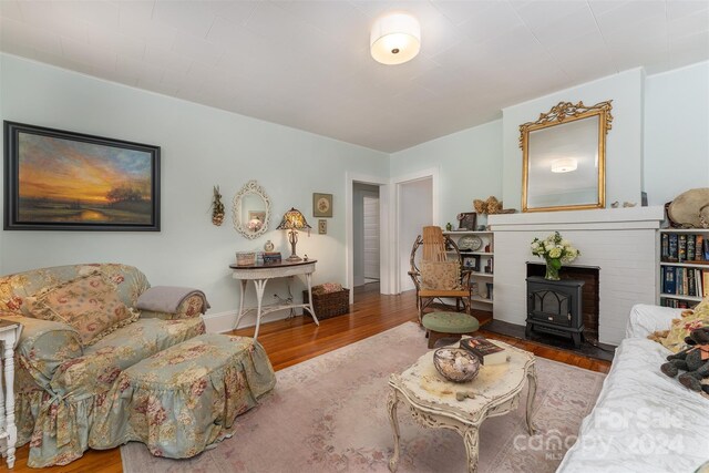 living room with wood-type flooring, a wood stove, and a brick fireplace