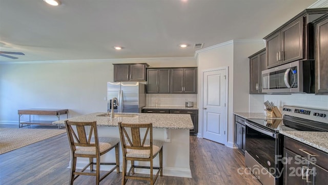 kitchen featuring appliances with stainless steel finishes, an island with sink, light stone countertops, dark hardwood / wood-style flooring, and ceiling fan