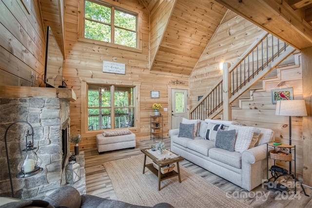 living room featuring a fireplace, high vaulted ceiling, light hardwood / wood-style flooring, wood walls, and wooden ceiling