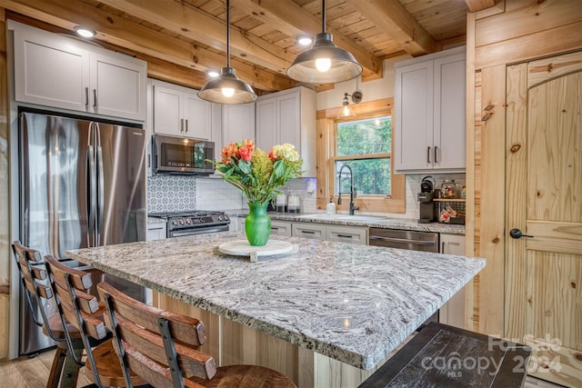 kitchen with a kitchen bar, a kitchen island, sink, appliances with stainless steel finishes, and beam ceiling