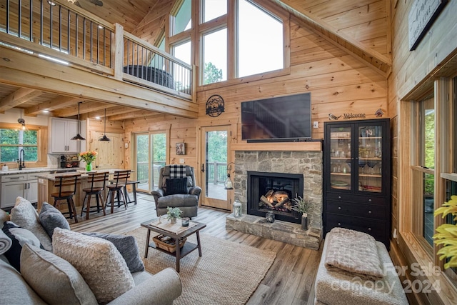 living room featuring wood ceiling, high vaulted ceiling, light hardwood / wood-style flooring, and a stone fireplace