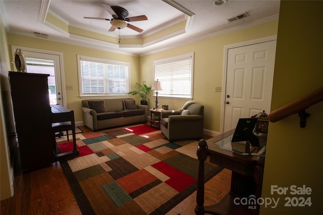 living room featuring dark hardwood / wood-style floors, ceiling fan, crown molding, and a tray ceiling