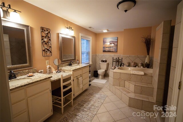 bathroom with vanity, tile patterned flooring, a relaxing tiled tub, and toilet