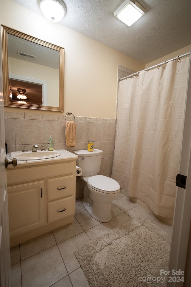 bathroom featuring tile patterned floors, vanity, a textured ceiling, tile walls, and toilet