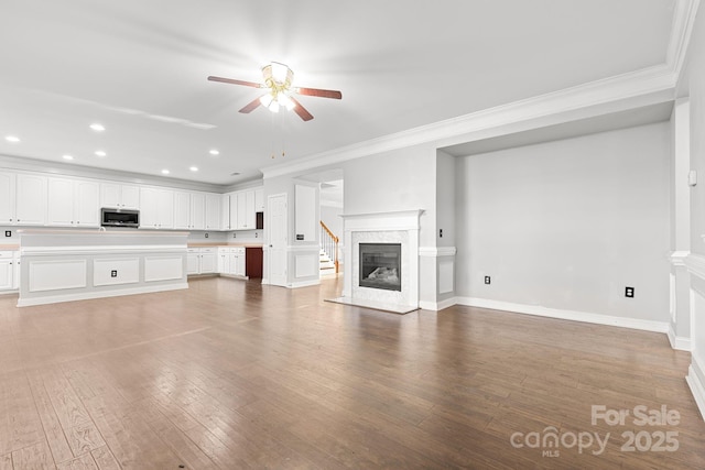 unfurnished living room with ceiling fan, wood-type flooring, crown molding, and a fireplace