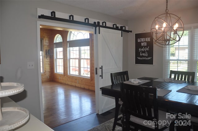 dining area featuring brick wall, a textured ceiling, a barn door, an inviting chandelier, and hardwood / wood-style floors