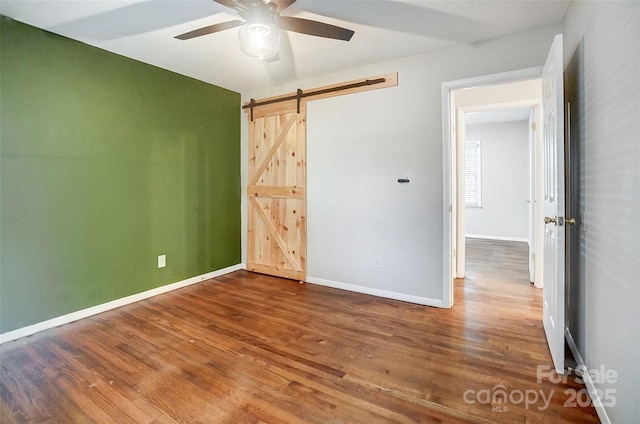 unfurnished bedroom featuring ceiling fan, hardwood / wood-style floors, and a barn door