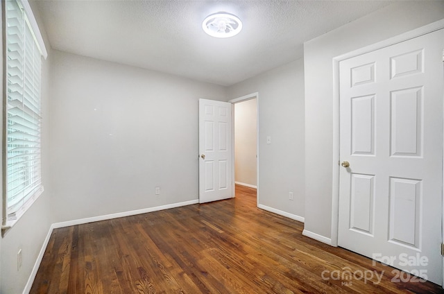 unfurnished bedroom featuring dark hardwood / wood-style floors, multiple windows, and a textured ceiling