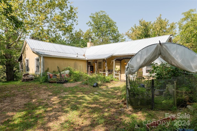 back of house with stucco siding, metal roof, and a chimney