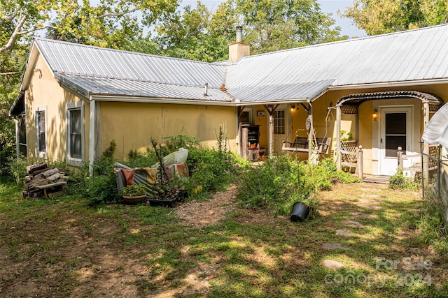 back of property with a chimney, stucco siding, and metal roof