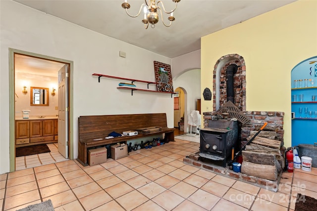 living room featuring an inviting chandelier, arched walkways, a wood stove, and light tile patterned flooring