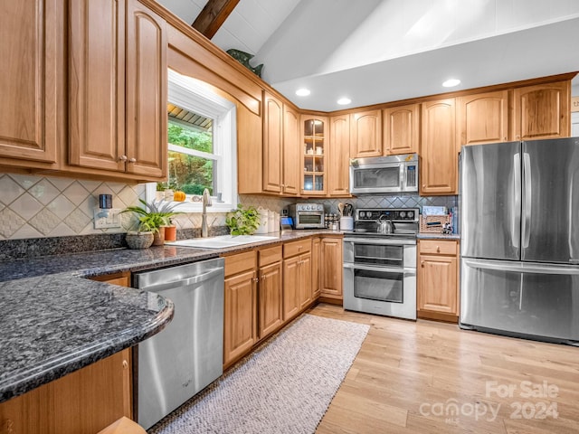 kitchen featuring light wood-type flooring, backsplash, stainless steel appliances, sink, and lofted ceiling with beams