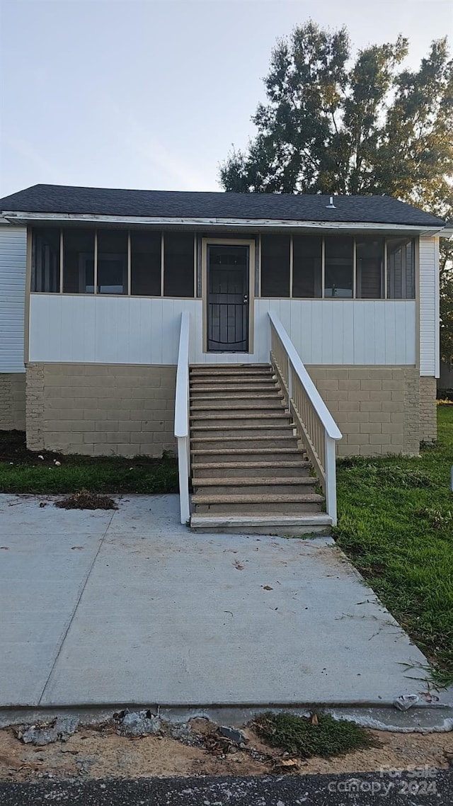 view of front facade featuring a sunroom, stairway, and roof with shingles