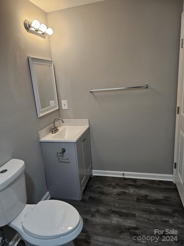 half bathroom with wood finished floors, vanity, toilet, and baseboards