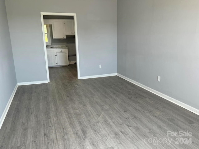 unfurnished bedroom with dark wood finished floors, a walk in closet, and baseboards