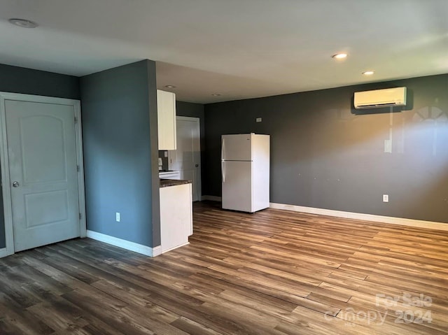 kitchen featuring a wall unit AC, dark countertops, dark wood-type flooring, freestanding refrigerator, and white cabinets