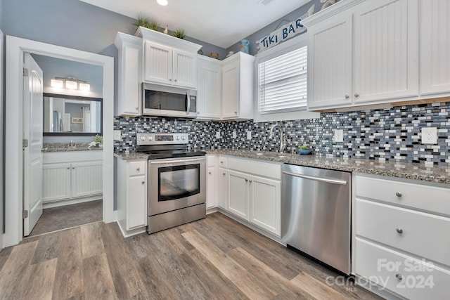 kitchen with tasteful backsplash, light stone counters, white cabinetry, light hardwood / wood-style floors, and stainless steel appliances