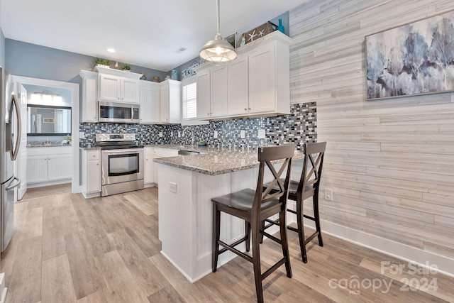 kitchen featuring light hardwood / wood-style floors, white cabinets, stainless steel appliances, and pendant lighting