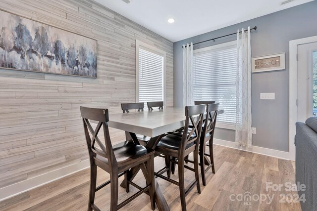 dining room featuring wooden walls, light hardwood / wood-style flooring, and a healthy amount of sunlight