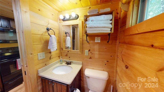 bathroom featuring wood ceiling, wooden walls, toilet, and vanity