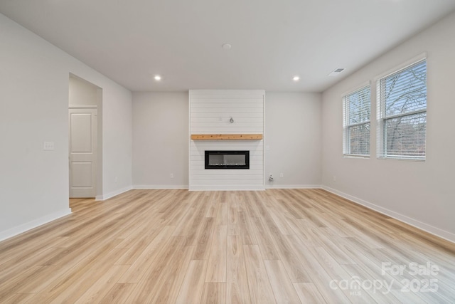 unfurnished living room with a large fireplace and light wood-type flooring