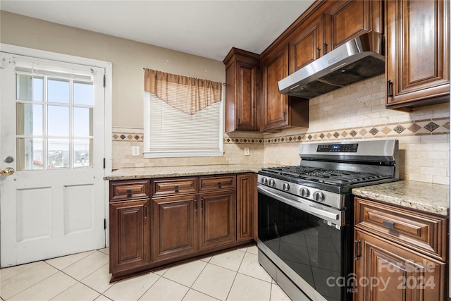 kitchen with light tile patterned floors, backsplash, stainless steel gas range, and light stone countertops