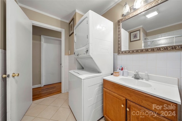 laundry room featuring light hardwood / wood-style flooring, stacked washing maching and dryer, ornamental molding, tile walls, and sink