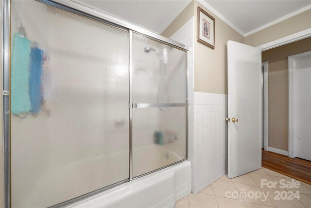 bathroom featuring hardwood / wood-style flooring, tile walls, crown molding, and bath / shower combo with glass door