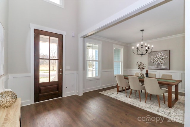 entrance foyer with dark wood-type flooring, a notable chandelier, crown molding, and wainscoting