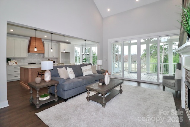 living room with dark wood-type flooring, high vaulted ceiling, recessed lighting, an inviting chandelier, and a fireplace