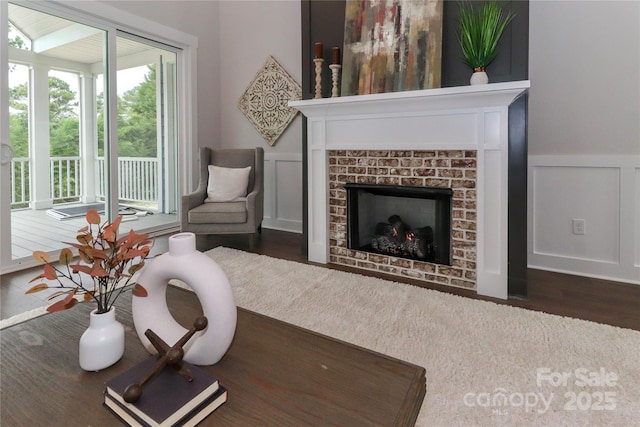 living room featuring wood finished floors, a decorative wall, a fireplace, and wainscoting