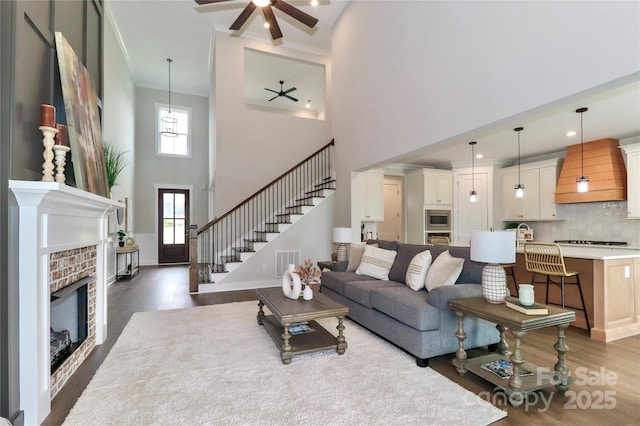 living area with visible vents, a brick fireplace, ceiling fan, dark wood finished floors, and stairway