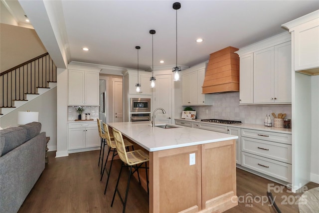 kitchen featuring a breakfast bar area, premium range hood, dark wood-style flooring, stainless steel appliances, and a sink