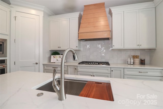 kitchen with a sink, backsplash, light stone countertops, and custom exhaust hood