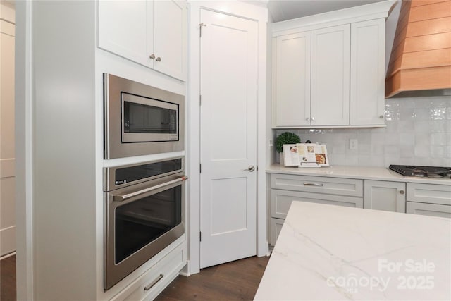 kitchen with stainless steel appliances, white cabinets, decorative backsplash, custom exhaust hood, and dark wood-style flooring