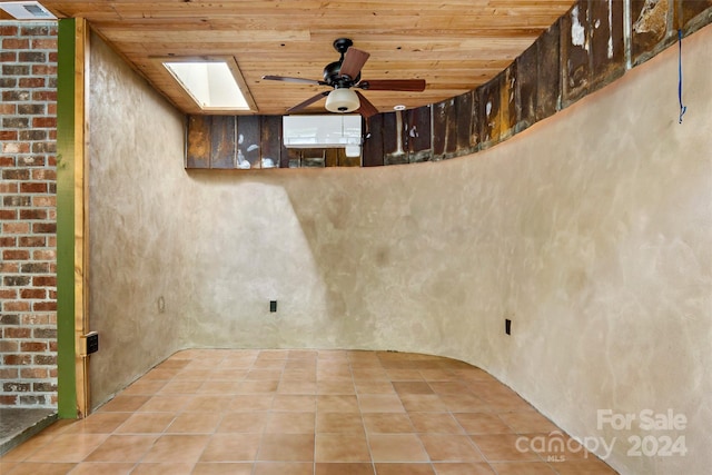 tiled empty room featuring wood ceiling, ceiling fan, and a skylight