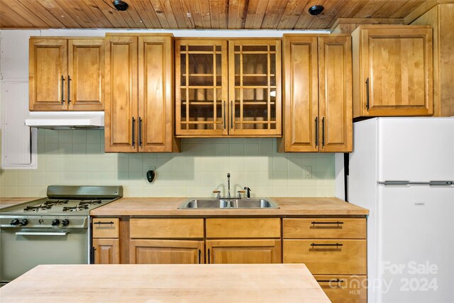 kitchen with wooden ceiling, wall chimney range hood, gas range oven, and white refrigerator